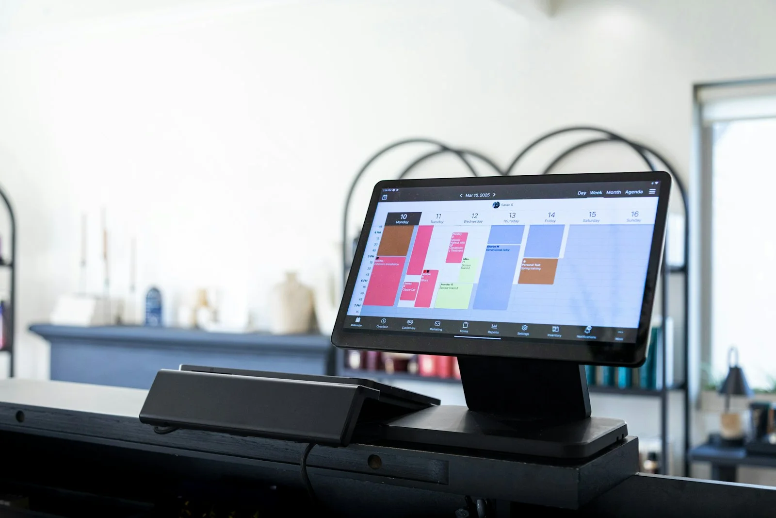 Tablet on a salon reception counter displaying a colourful weekly appointment calendar for small business scheduling